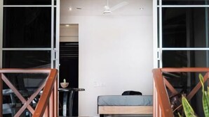 Un escalier menant à une pièce où se trouvent un lit, une petite table et un ventilateur de plafond.