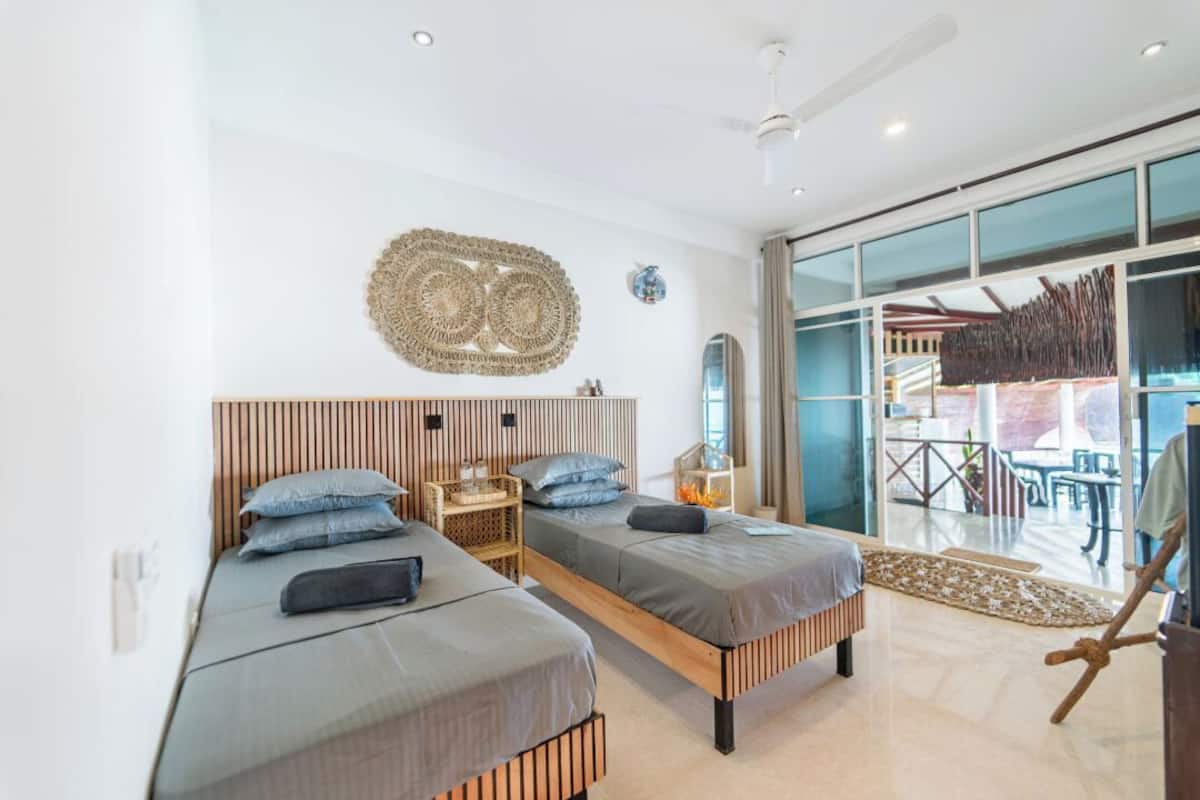 A modern bedroom with two beds, a large window, and a decorative wall piece.