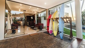 Un intérieur moderne avec une porte vitrée donnant sur un patio. À l’intérieur, on trouve des planches de surf accrochées à un support, un canapé et une petite table agrémentée d’un objet décoratif.