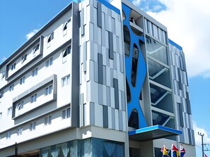 Un edificio de varios pisos con un diseño arquitectónico moderno, que destaca por una llamativa combinación de colores azul y blanco y una fachada central de vidrio.