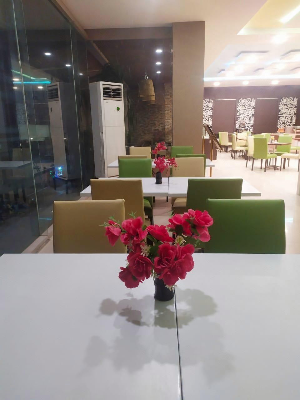 En restaurant med hvide borde og grønne stole, en vase med røde blomster på et bord, og et moderne interiør.
