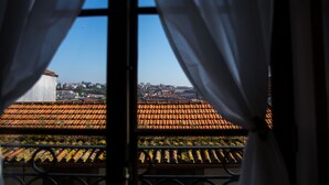 A view through a window with curtains, displaying a tiled roof and a distant cityscape. - Belos Aires Apartments (Porto)