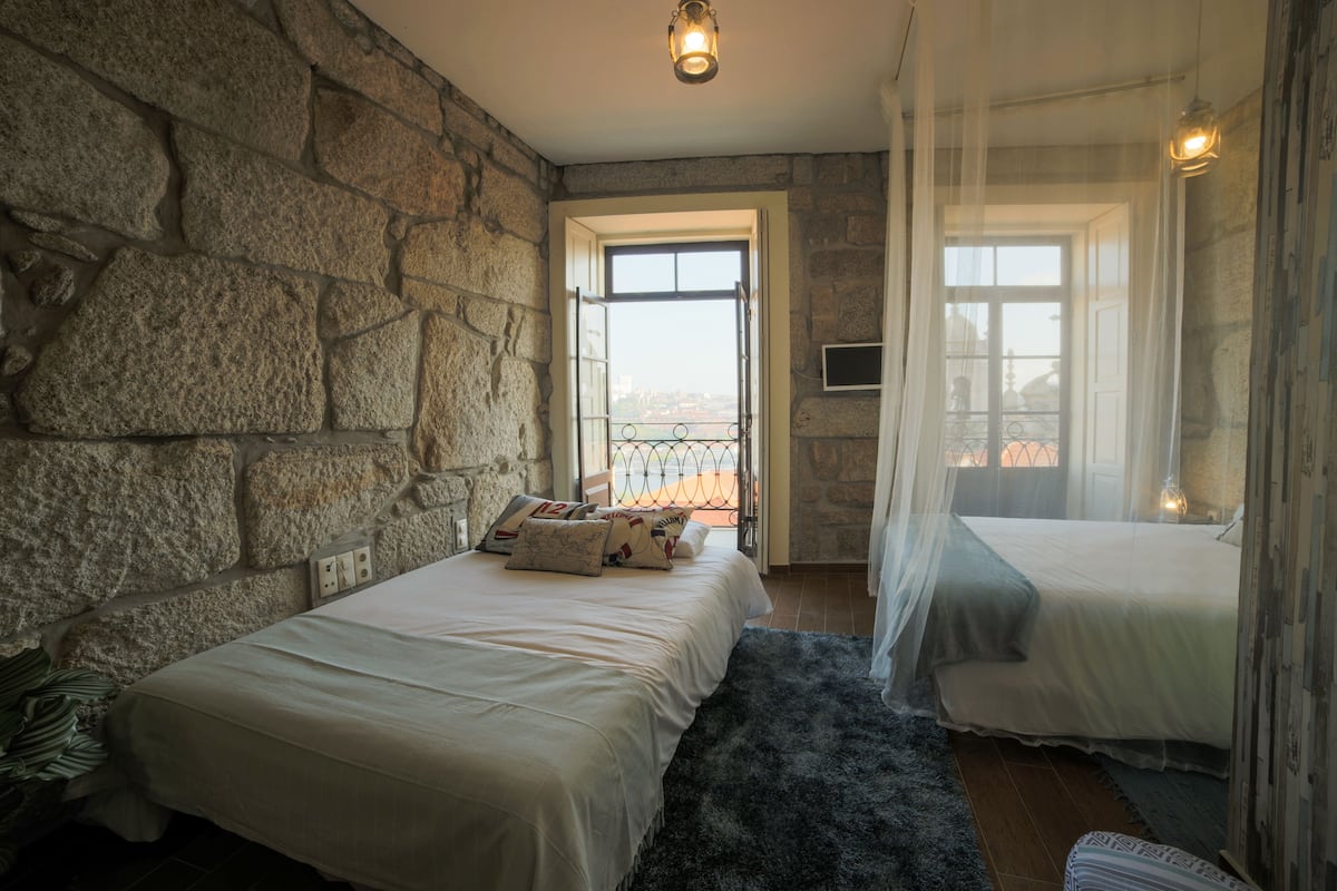 Un dormitorio con dos camas, paredes de piedra, un ventanal y vistas a la ciudad.