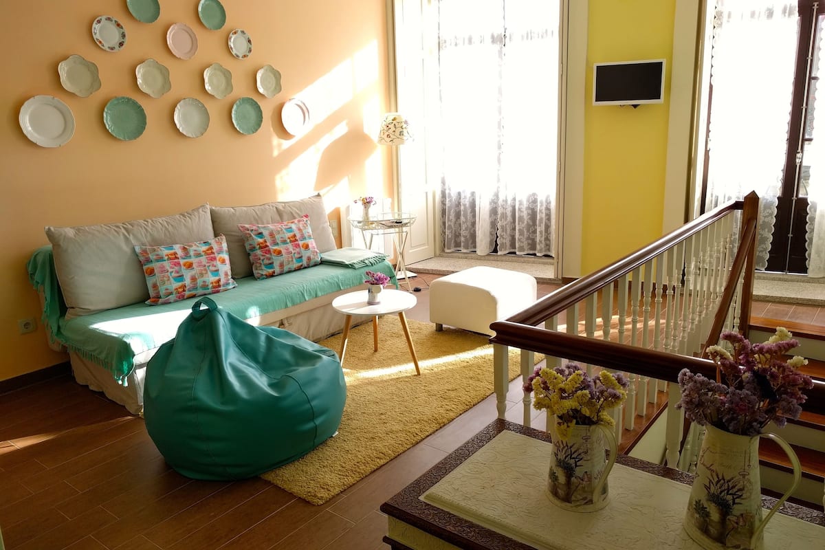 Un salón con un sofá, un sillón de peluche verde, una mesita de centro y un jarrón con flores.