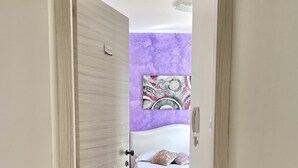 A hallway leading to a bedroom with a bed, a purple wall, and a ceiling fan. - Bella Tropea Accommodation (Tropea)