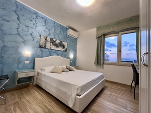 Une chambre à coucher comprenant un lit, une table de chevet, une chaise, une fenêtre avec des rideaux et un climatiseur fixé au mur.
