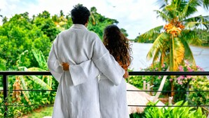 Una pareja parada en un balcón con vistas a un exuberante jard ín, un río y palmeras.