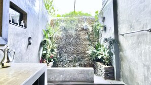 Un espacio reducido y cerrado con pared de piedra, plantas en macetas y un pequeño elemento de agua.