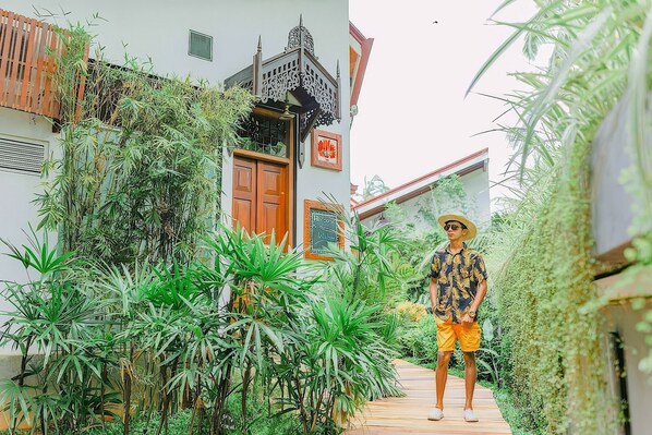 A narrow pathway flanked by lush greenery and a building with a traditional design, including a wooden door and a signboard. - Waterland (Negombo)