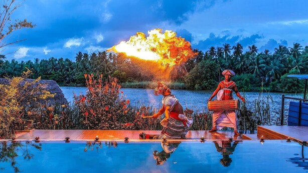 Zona junto a la piscina con un espectáculo de fuego, palmeras y una masa de agua tranquila al fondo.