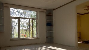 Ein Zimmer mit großem Fenster, Holzboden und einer weißen Wand mit integriertem Regal.