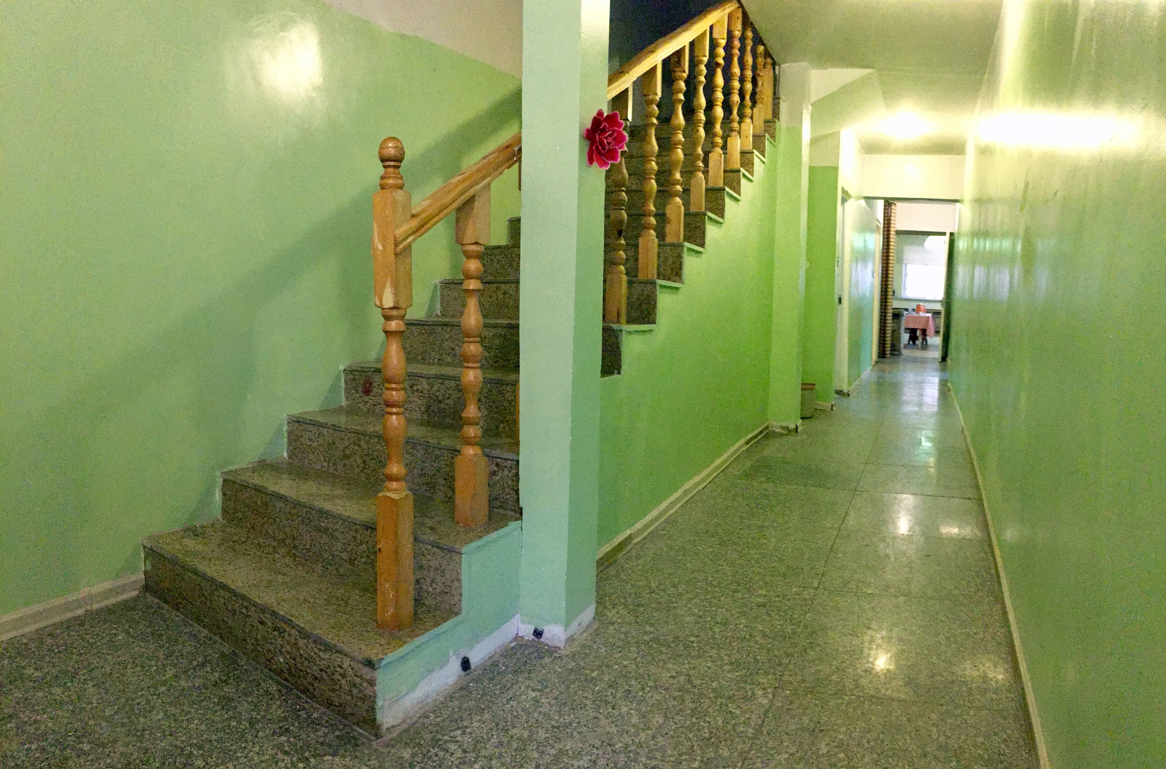 Escadaria com balaústres de madeira e degraus de granito, que leva a um patamar decorado com uma flor vermelha.