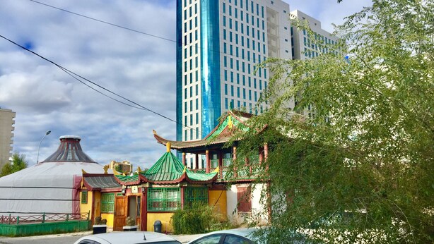 Ein traditionelles Gebäude mit grüner Dachbegrünung und roten Akzenten, neben einem modernen Hochhaus.