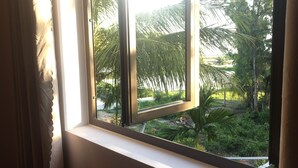 A window with a view of a garden with palm trees and other greenery. - Tra Que Riverside Homestay (Da Nang)