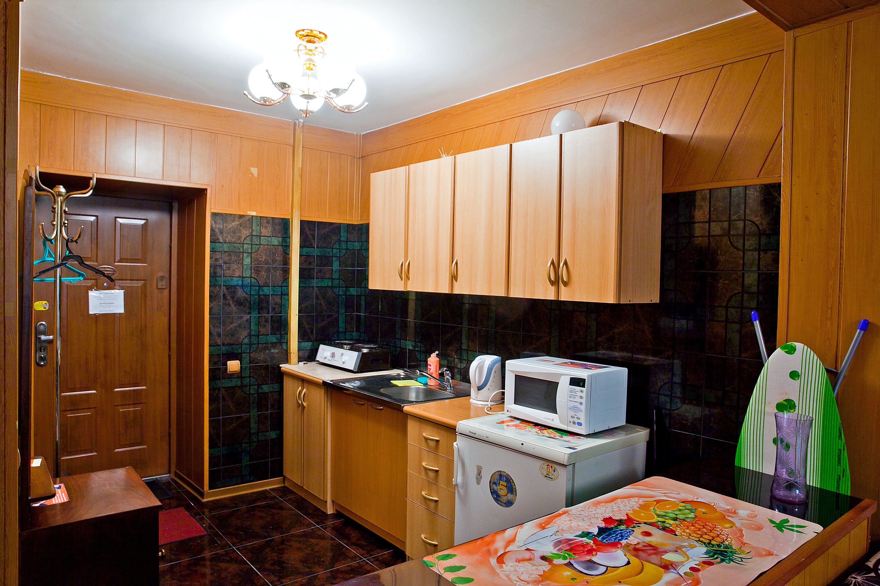 Uma cozinha compacta com armários de madeira, micro-ondas, geladeira pequena e painel atrás do fogão revestido de azulejos.