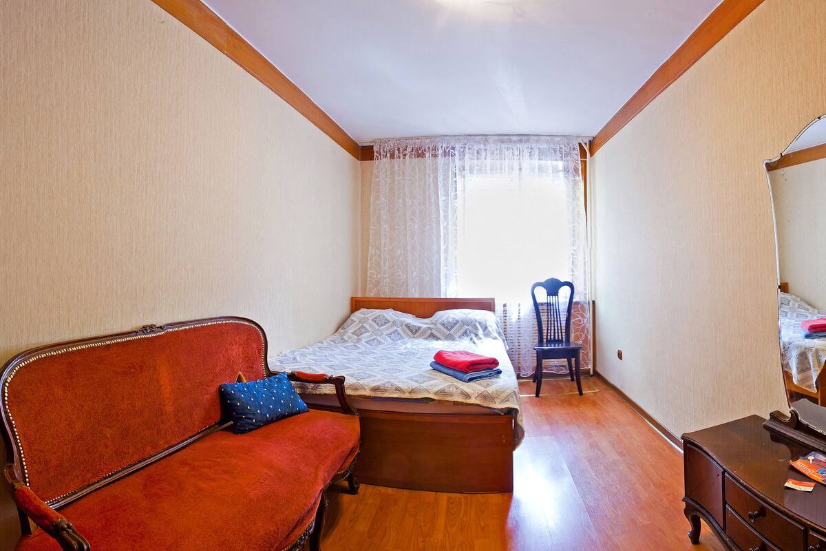 A bedroom with a wooden bed, a red sofa, a wooden dresser, and a chair.