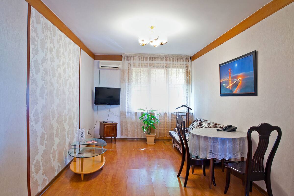 A dining area with a round table, chairs, a potted plant, and a television on the wall.