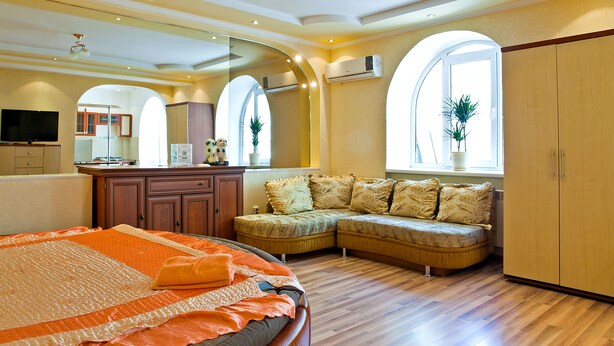 A bedroom with a bed, a seating area, a wardrobe, and a television. - Lessor Apartments (Almaty)