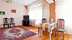 A dining area with a table set for two, two chairs, a television, and a decorative rug. - Lessor Apartments (Almaty)