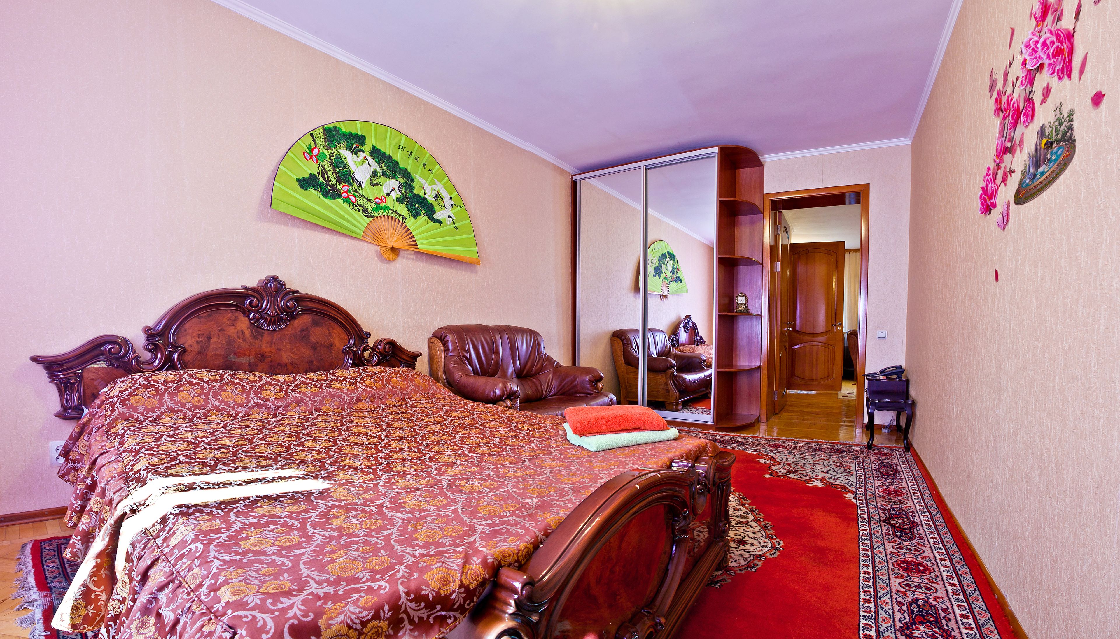 A bedroom with a large bed, a wooden chair, a mirror, and a traditional fan.