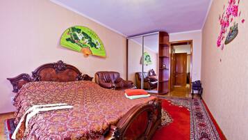 A bedroom with a large bed, a wooden chair, a mirror, and a traditional fan.