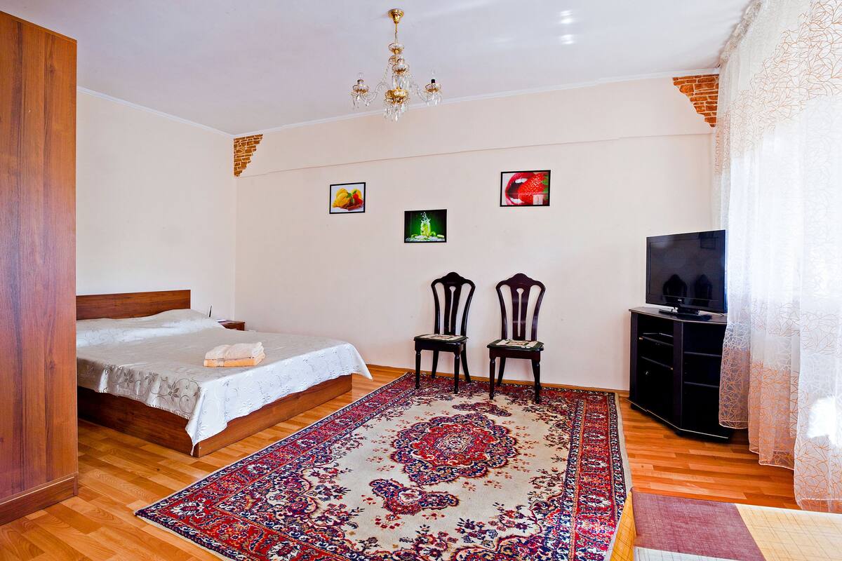 A bedroom with a bed, two chairs, a TV stand, and a large rug.