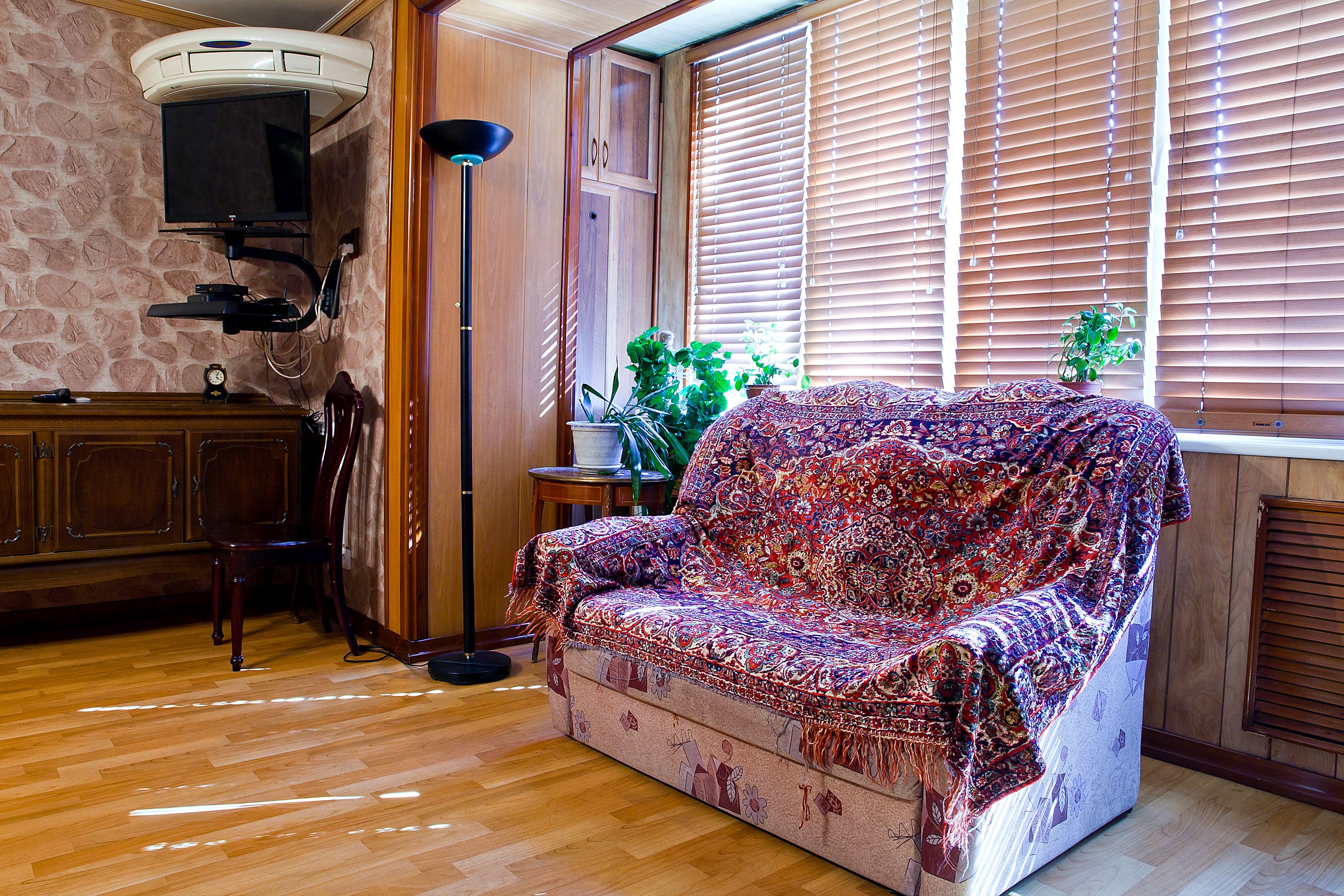 A cozy living room with a patterned sofa, a television mounted on the wall, a wooden cabinet, and a potted plant by the window.