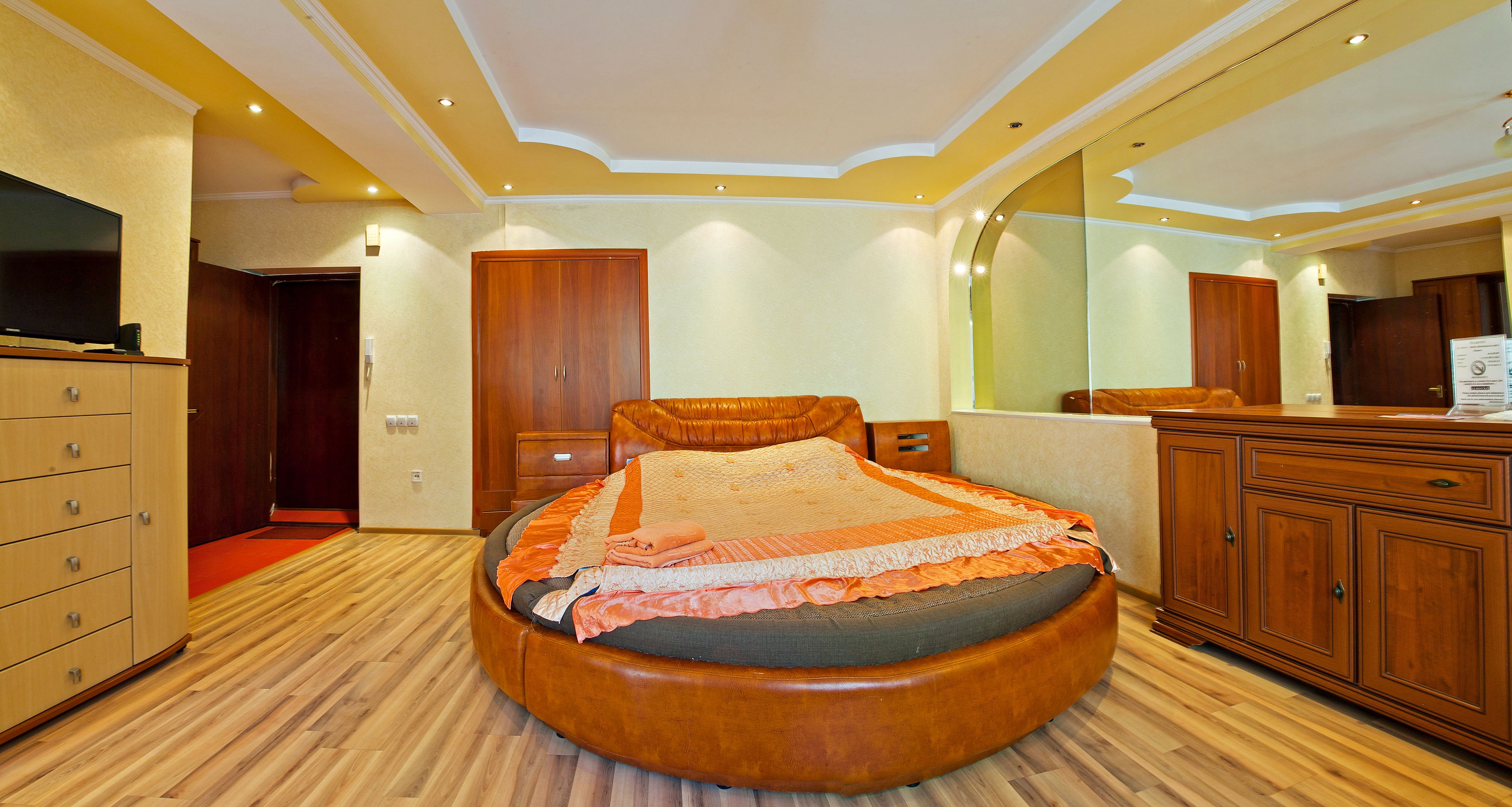 Una camera da letto ben illuminata con un letto rotondo, un'armadiatura in legno e un grande specchio.