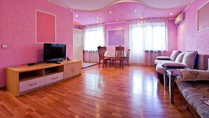 A pink-themed living room with a TV, wooden furniture, and a dining area. - Lessor Apartments (Almaty)