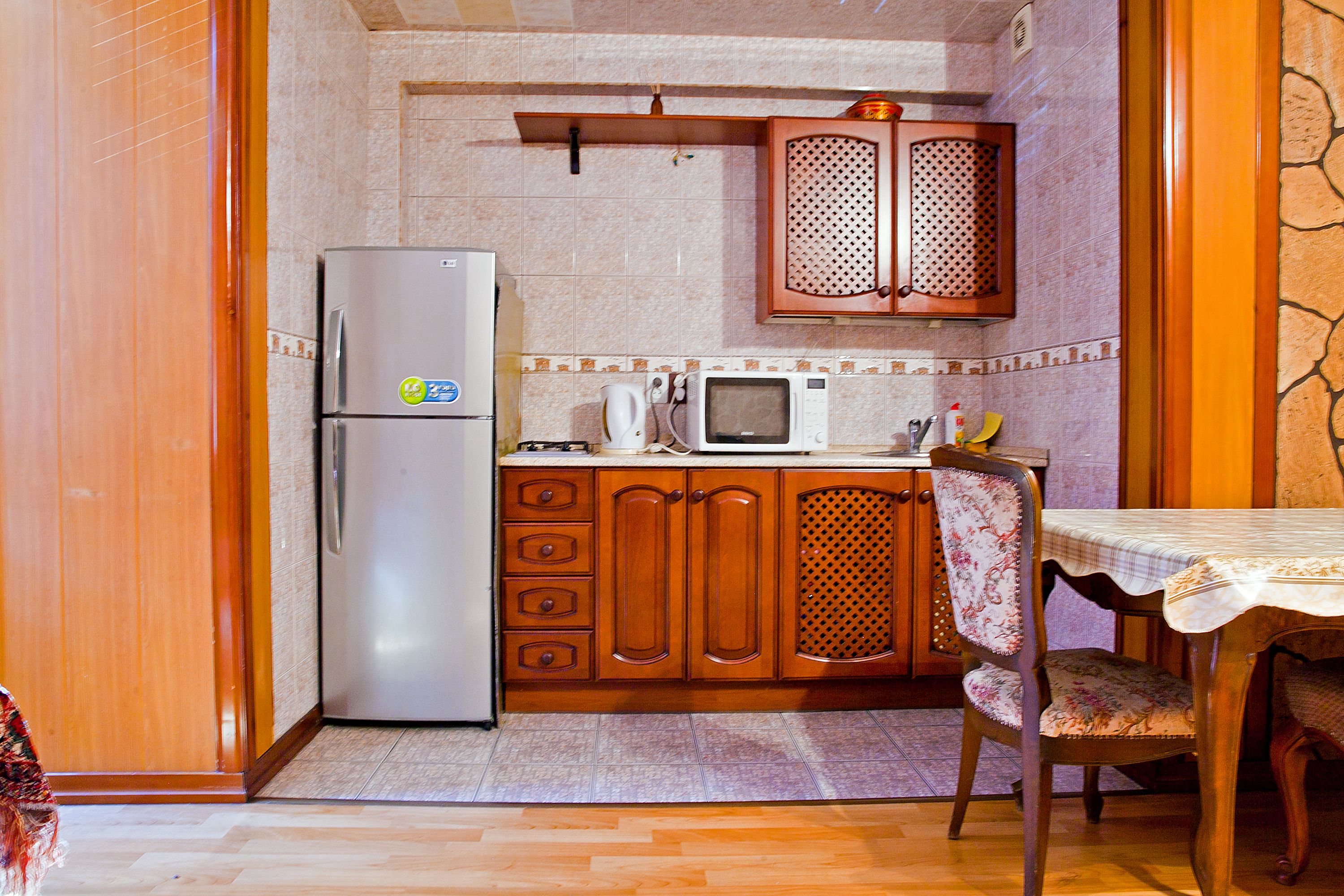A compact kitchen with wooden cabinets, a refrigerator, a microwave, and a dining table with a chair.