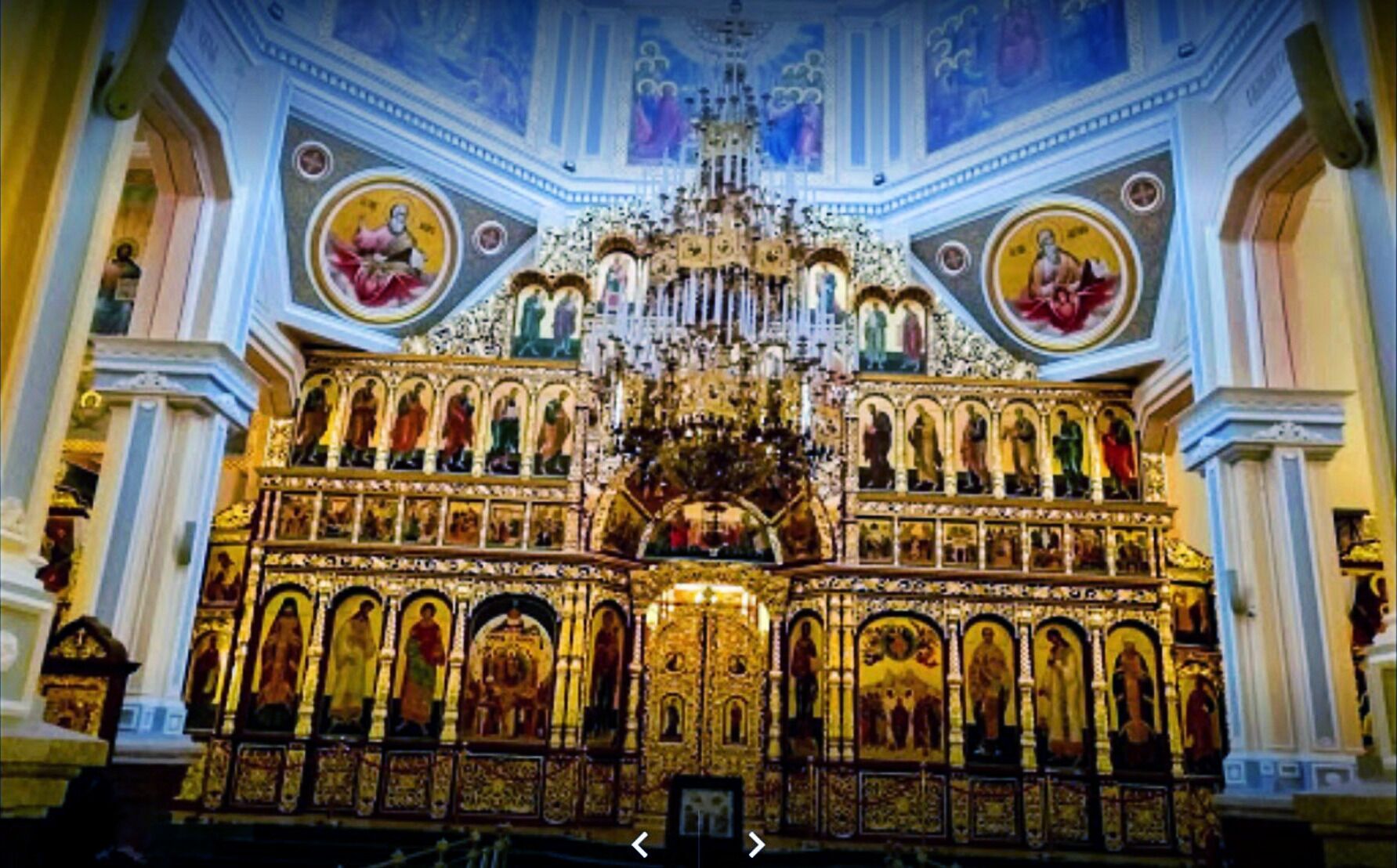 An ornate church interior with a central altar, multiple altars, and a large chandelier.