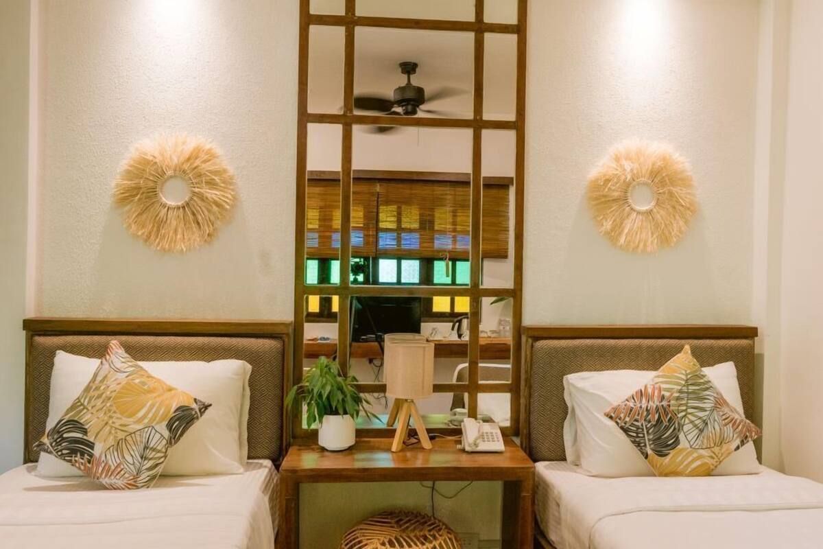 Une chambre d’hôtel avec deux lits, une table de chevet en bois avec une lampe, un téléphone et une petite plante en pot.