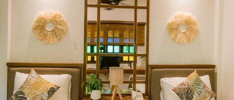 A hotel room with two beds, a wooden nightstand with a lamp, a telephone, and a small potted plant.