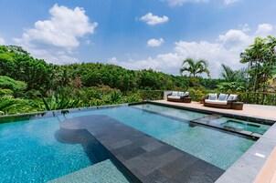 A rectangular infinity pool with clear water, surrounded by a wooden deck and a seating area with two sofas and cushions.