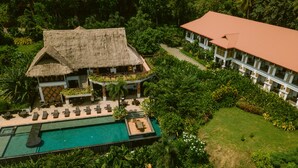 Vista aerea di un resort con piscina, area relax e un edificio dal tetto rosso.
