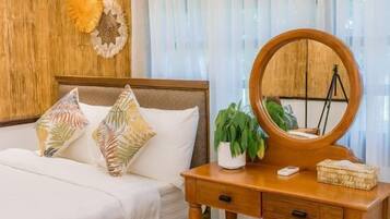Un dormitorio con cabecera de madera, cama con ropa de cama blanca, cómoda de madera con espejo y un taburete de mimbre.
