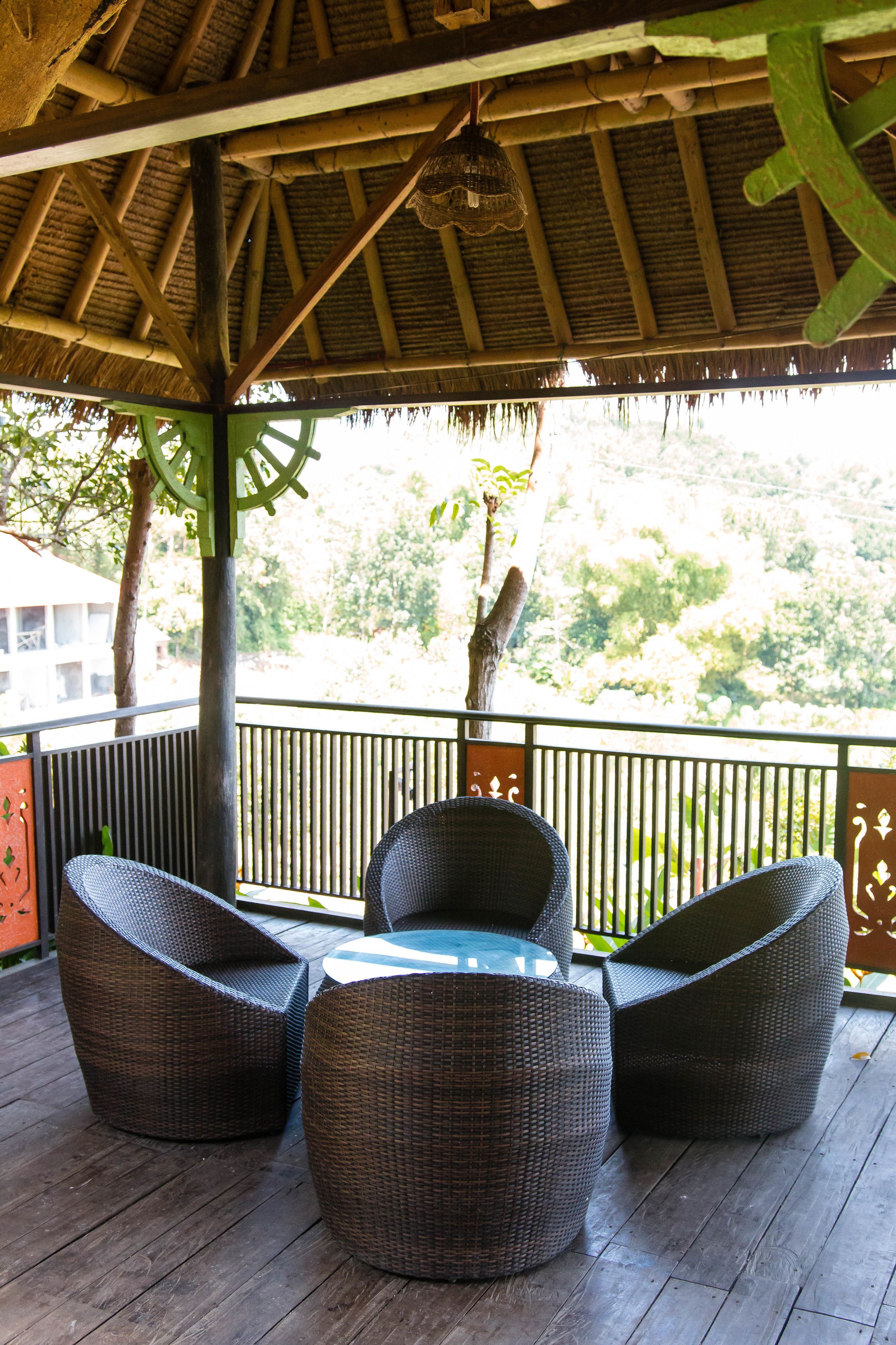 Un área de estar al aire libre, techada, con mobiliario de mimbre y vistas a un paisaje exuberante.