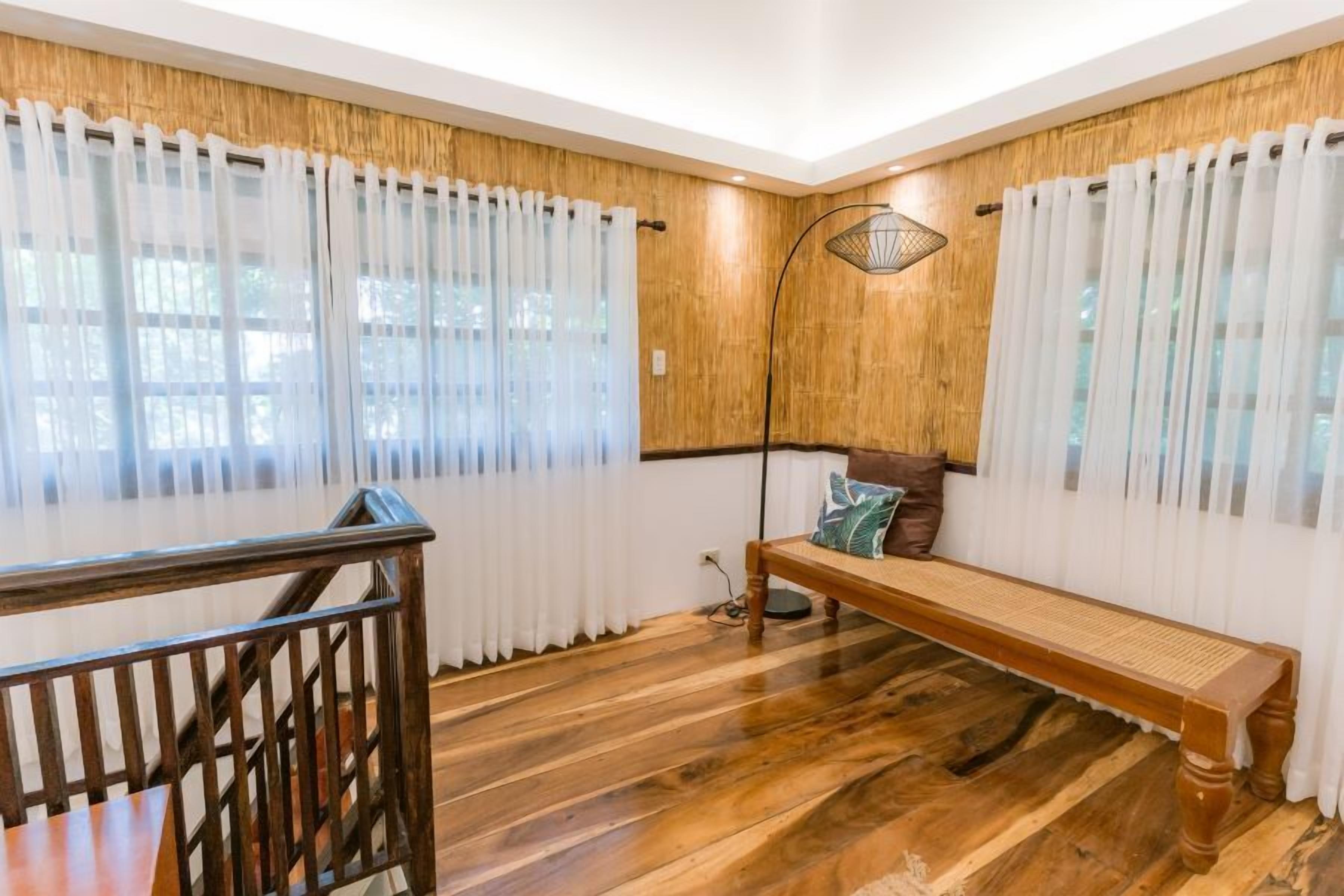 A room with a wooden floor, a bench with cushions, a wooden railing, and a wall-mounted lamp.