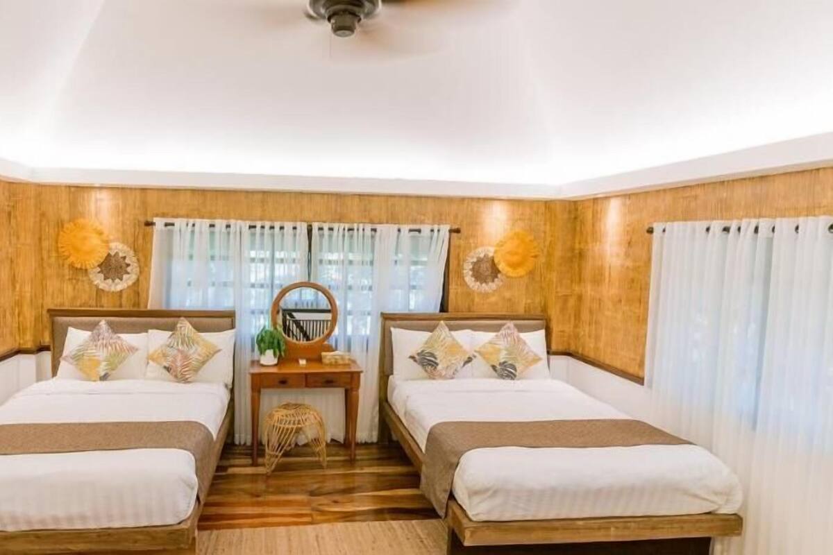 Une chambre avec deux lits, une tête de lit en bois, une petite table avec un miroir et une fenêtre avec des rideaux.