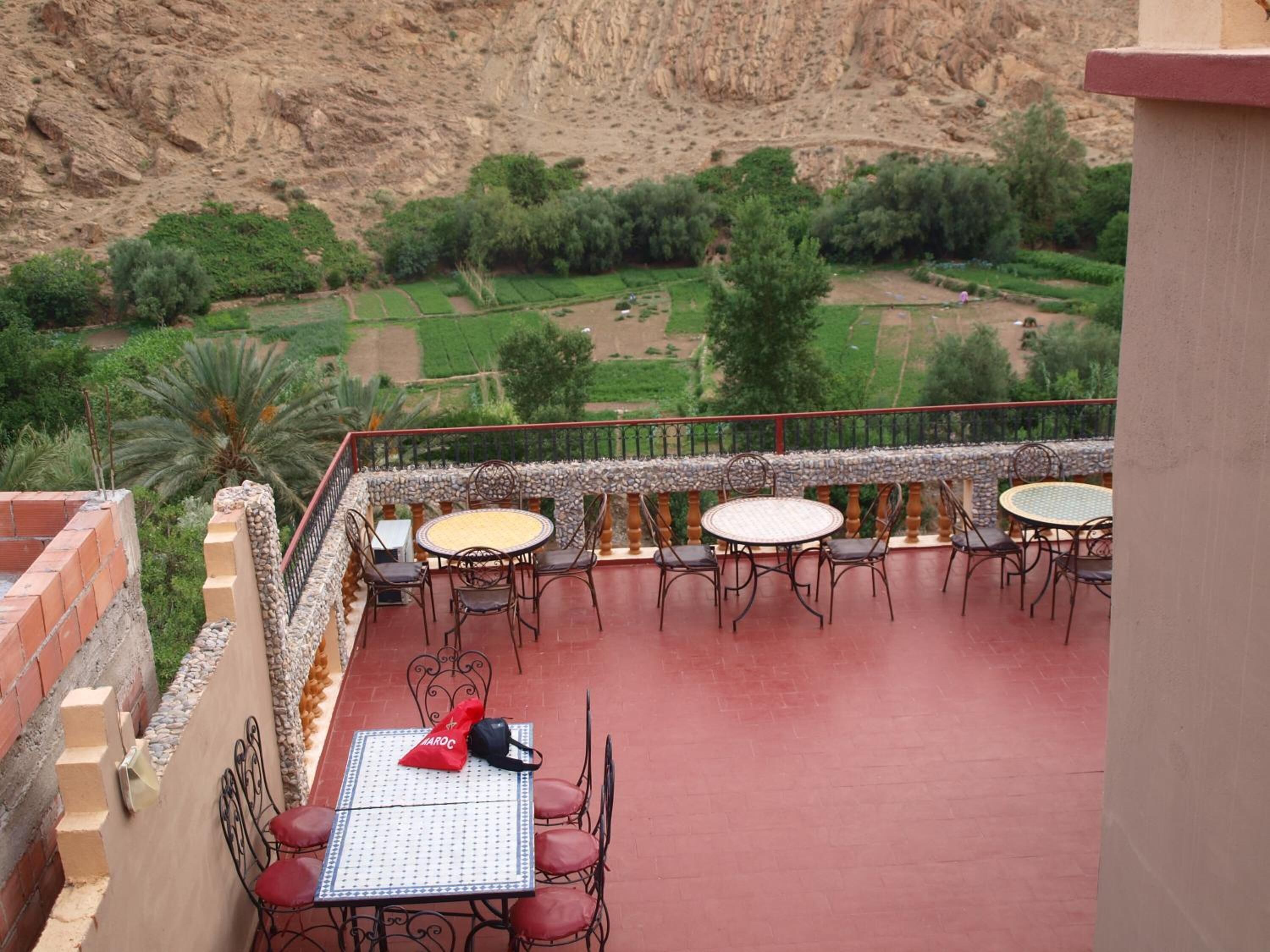 Una terraza con mesas y sillas, con vistas a un jardín ajardinado y una ladera rocosa.