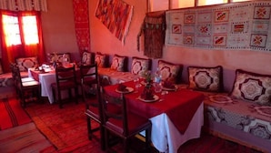 A dining area with a red tablecloth, wooden chairs, and patterned cushions. - Maison d'hôtes Valentine (Toudgha El Oulia)