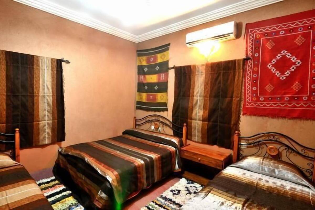 Quarto com duas camas, um objeto pendurado na parede e um ventilador de teto.