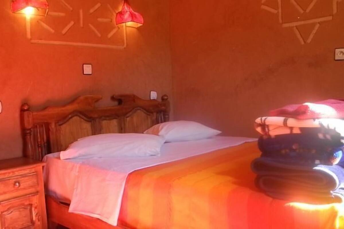 Um quarto com uma cama de madeira, duas mesas de cabeceira e duas luminárias fixadas na parede.