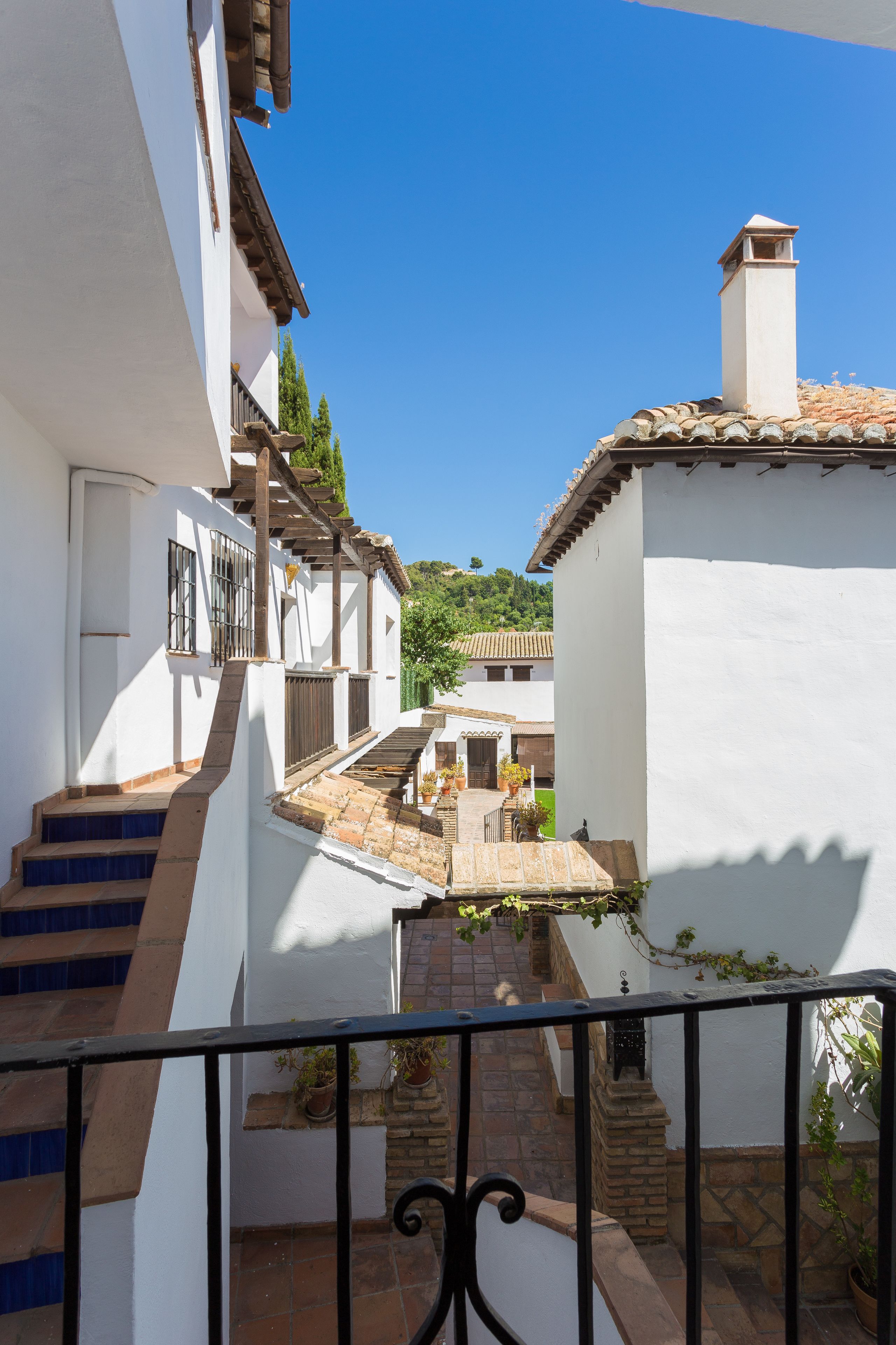 Une ruelle étroite bordée de bâtiments blancs, avec un escalier et une vue sur une colline.