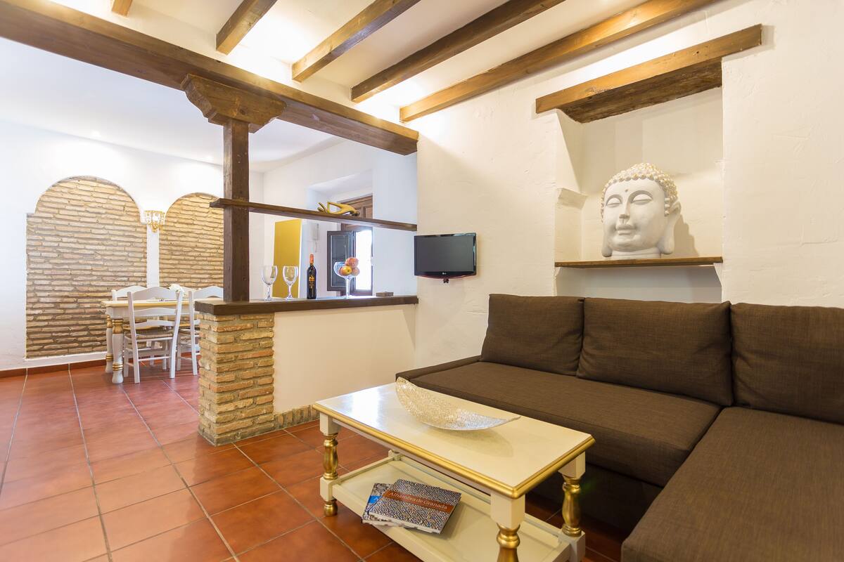 Una sala de estar con un sofá marrón, una mesa de centro blanca y una pared de piedra.
