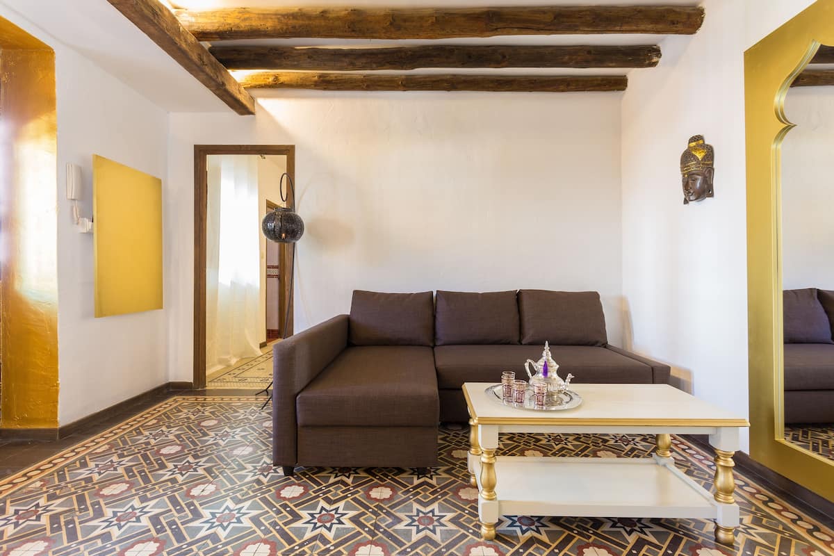 Una sala de estar con un sofá marrón, una mesa de centro blanca y un suelo estampado.