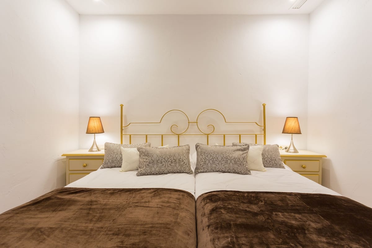 Una cama doble con una colcha marrón, dos mesitas de noche con lámparas y un cabecero decorativo.