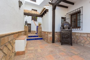 Un patio con una escalera de piedra que lleva a una puerta, un soporte metálico decorativo y una ventana con barrotes.