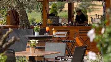 Ein Straßencafé mit Holztischen und -stühlen, einer Bar mit Barkeeper und Blick auf die Landschaft.