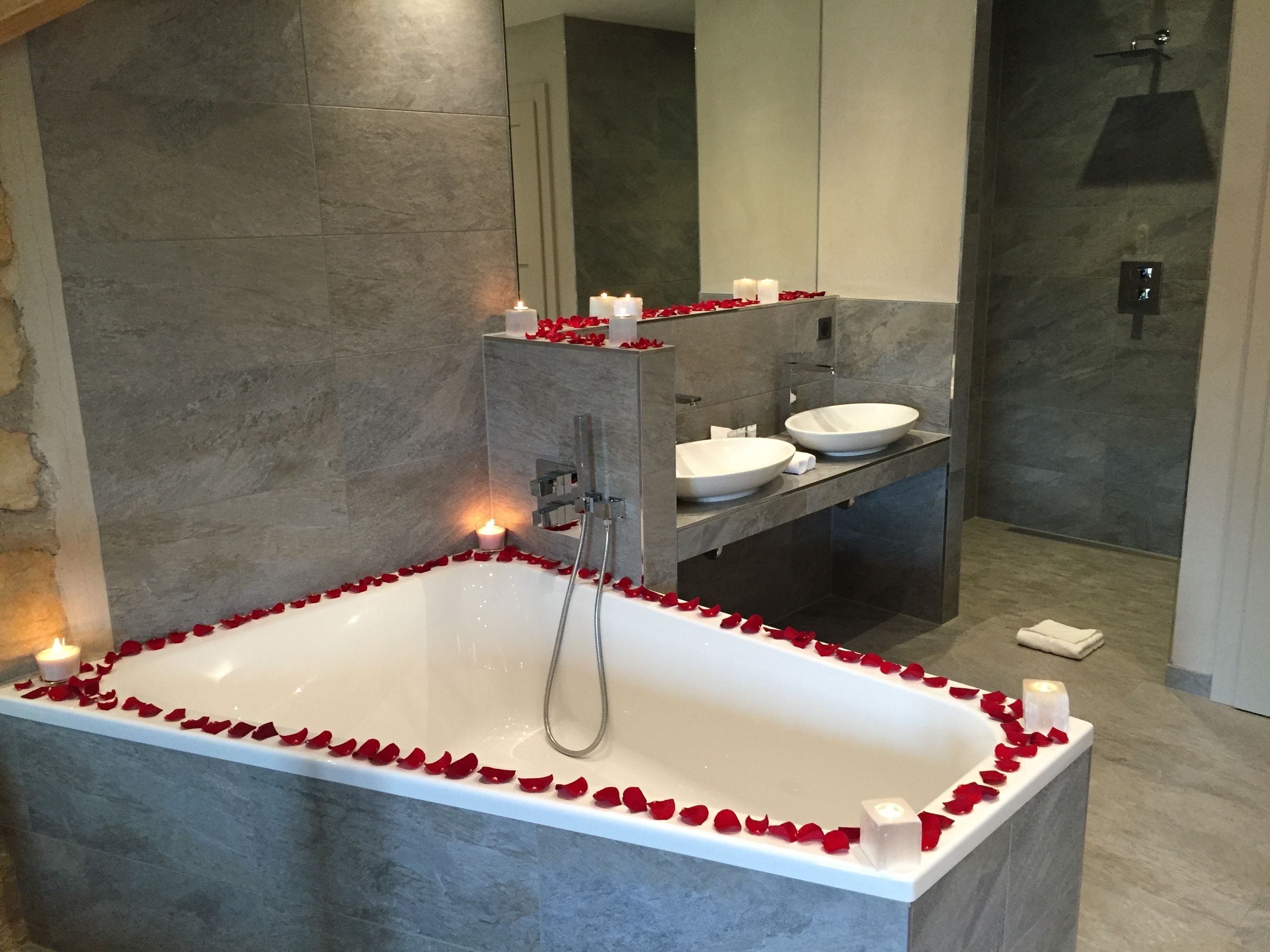 Un baño moderno con una bañera independiente rodeada de pétalos de rosa, un espejo grande y una zona de ducha.